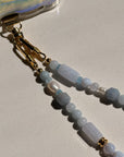 Beaded keychain with gold clasp on a light quartz background with pearls.