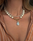 Pearl necklace with a large pendant worn by a person against a neutral background