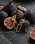 Gold chain earring on a dark surface with halved figs