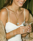 Woman in a white dress holding a martini glass with a fur coat and jewelry.