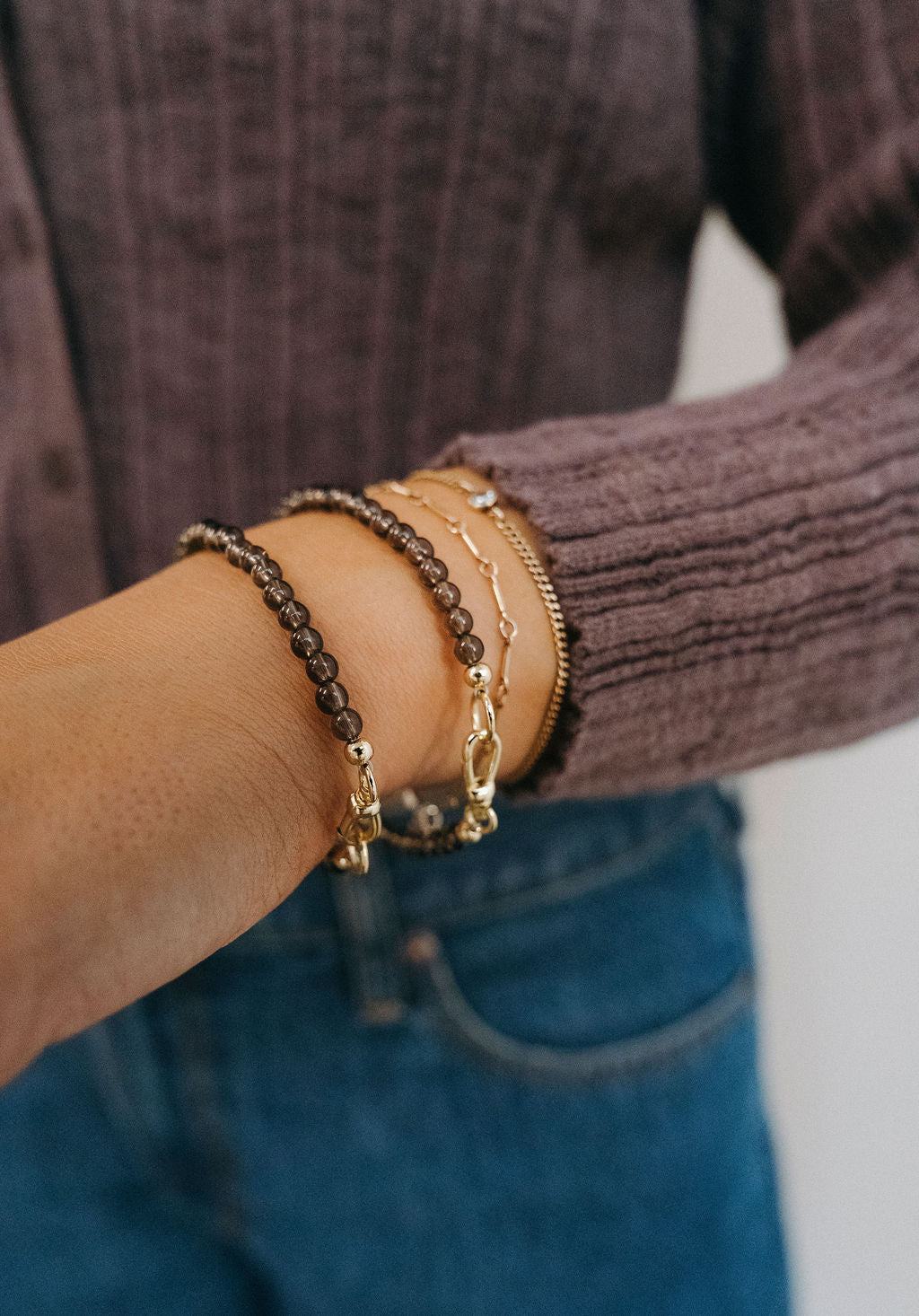 Close-up of a wrist wearing multiple gold bracelets with a blurred background