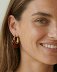 Close-up of a woman wearing gold hoop earrings with a neutral background