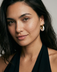 Woman wearing gold and pearl earrings against a neutral background