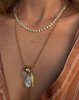 Close-up of a person wearing a gold necklace with a pearl pendant and fish charm.