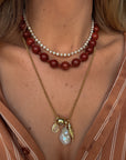 Close-up of a woman wearing a red beaded necklace and a gold chain with a pendant.