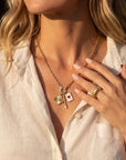 Woman wearing a gold necklace with charms and rings on a blurred background