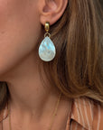 Close-up of a woman wearing a gold earring with a teardrop-shaped pearl-like stone.