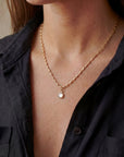 Gold necklace with a pearl pendant worn by a person in a black shirt.