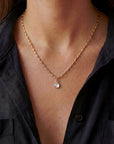 Gold necklace with a pendant worn by a person in a black shirt.