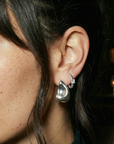 Close-up of a woman's ear wearing a silver earring with a blurred background