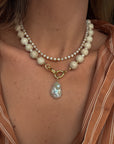 Pearl necklace with a gold clasp worn by a person, with a blurred background.