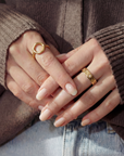 Close-up of hands with gold rings wearing a brown sweater and blue jeans.