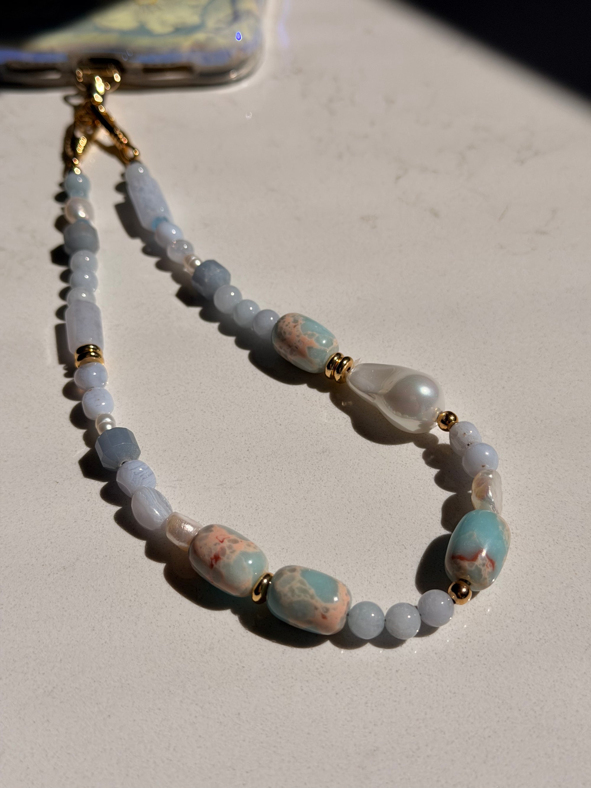 Beaded phone lanyard with pearls and gold accents on a light surface