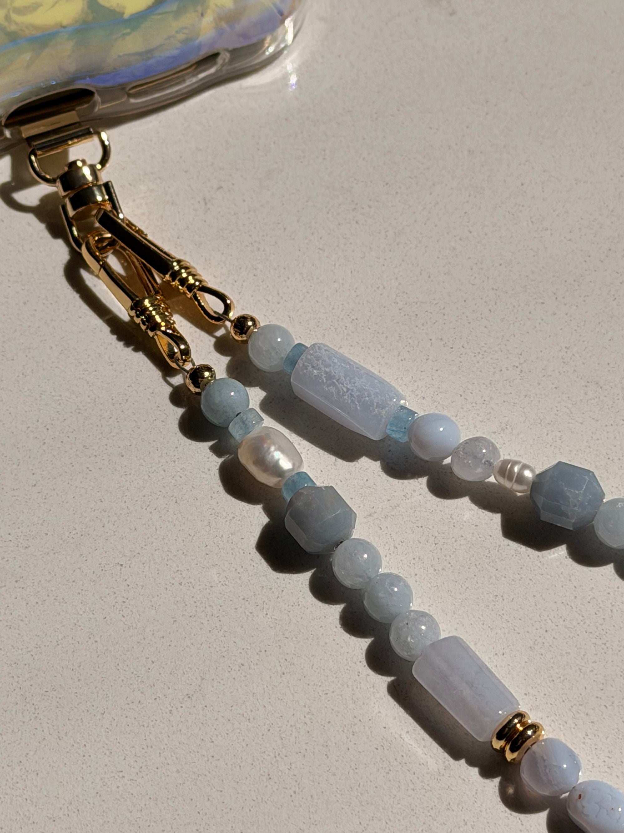 Beaded keychain with gold clasp on a light quartz background with pearls.