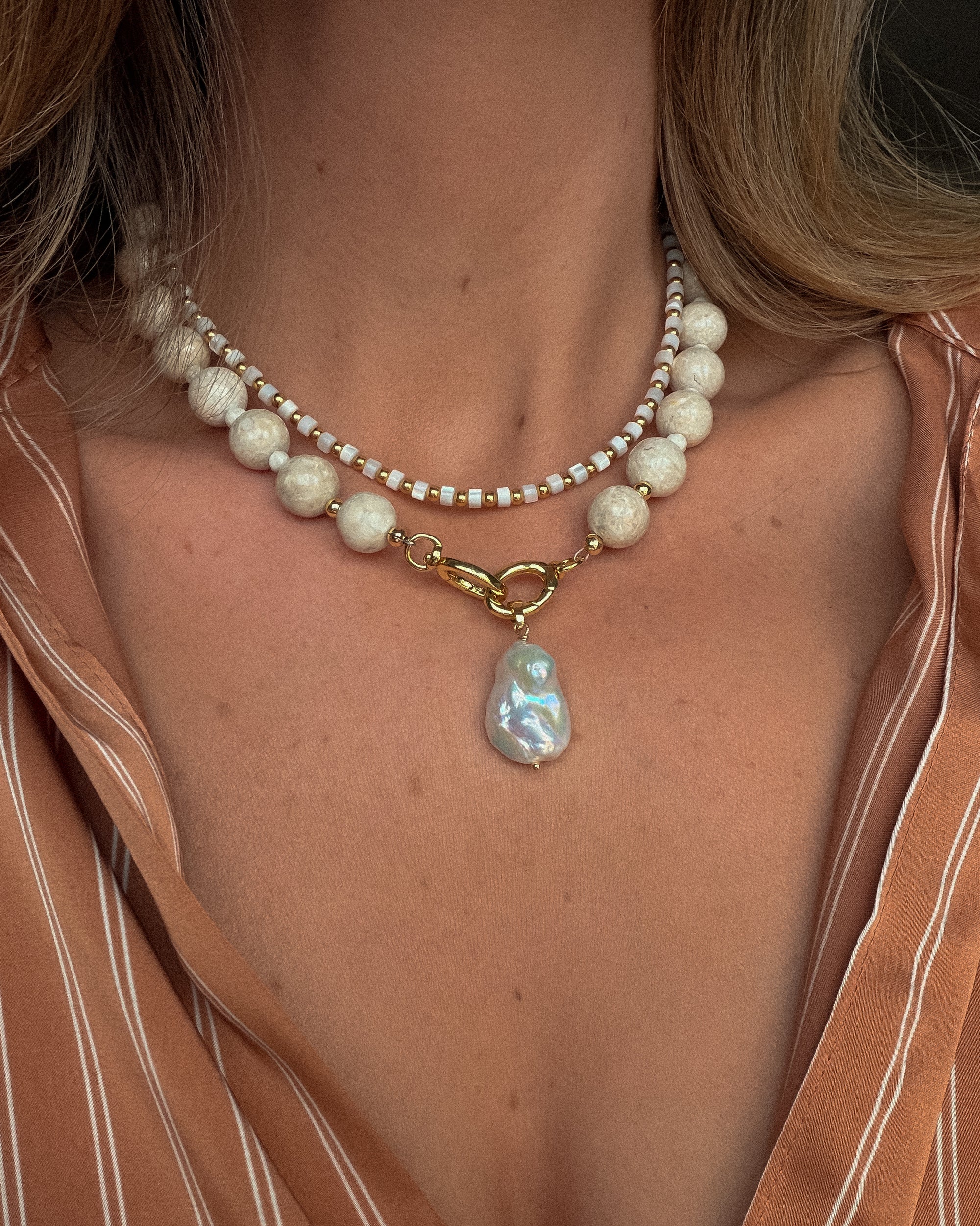 Pearl necklace with a large pendant worn by a person against a neutral background