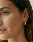 Close-up of a woman wearing a gold earring with a neutral background
