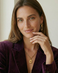 Woman wearing a purple blazer and gold jewelry indoors