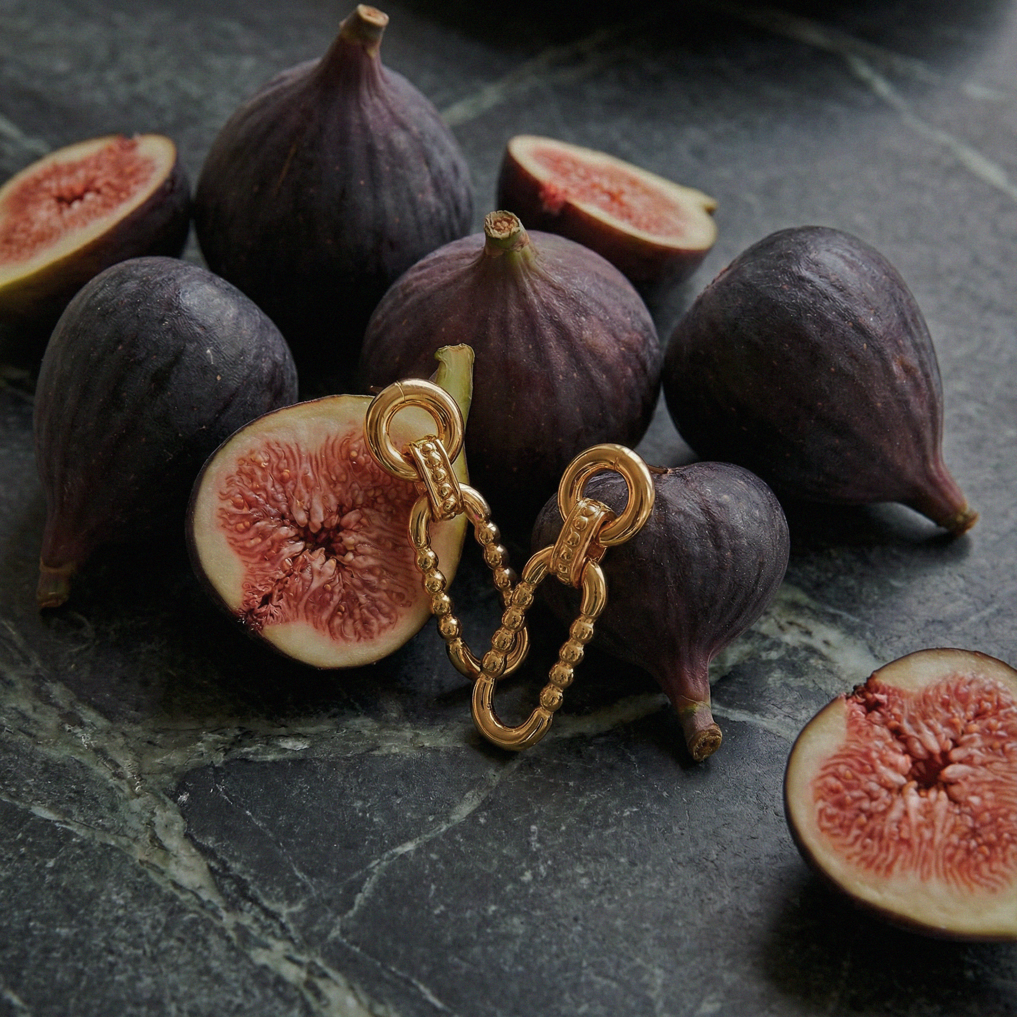 Gold chain earring on a dark surface with halved figs