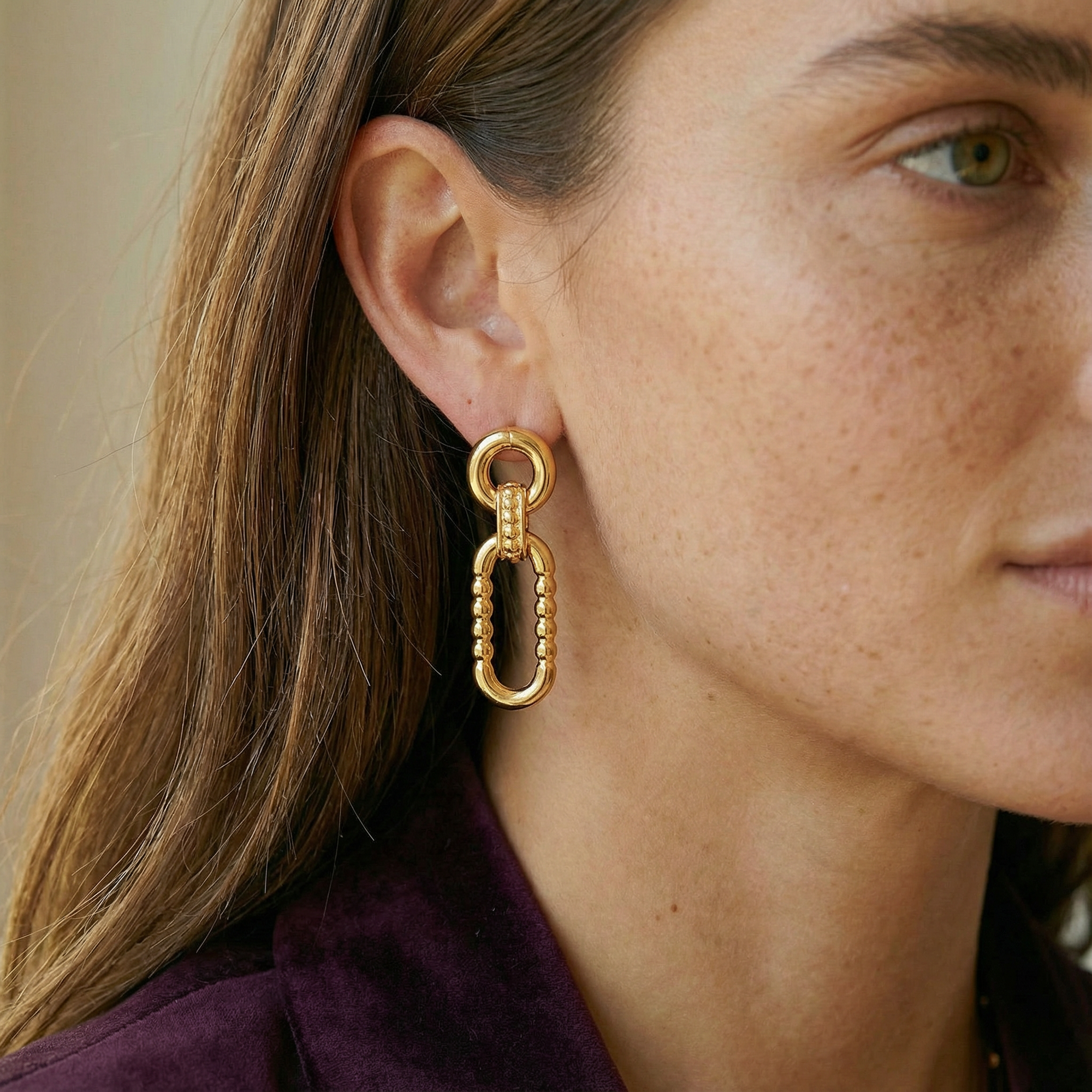 Close-up of a woman wearing gold earrings with a neutral background