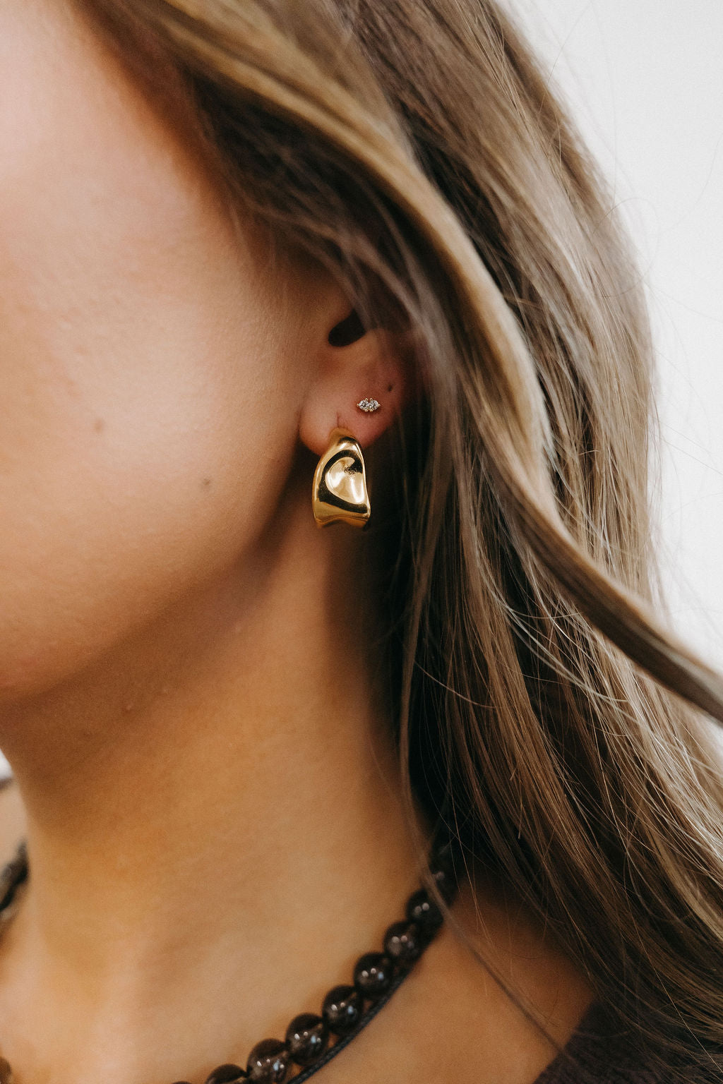 Close-up of a person wearing gold hoop earrings with a blurred background