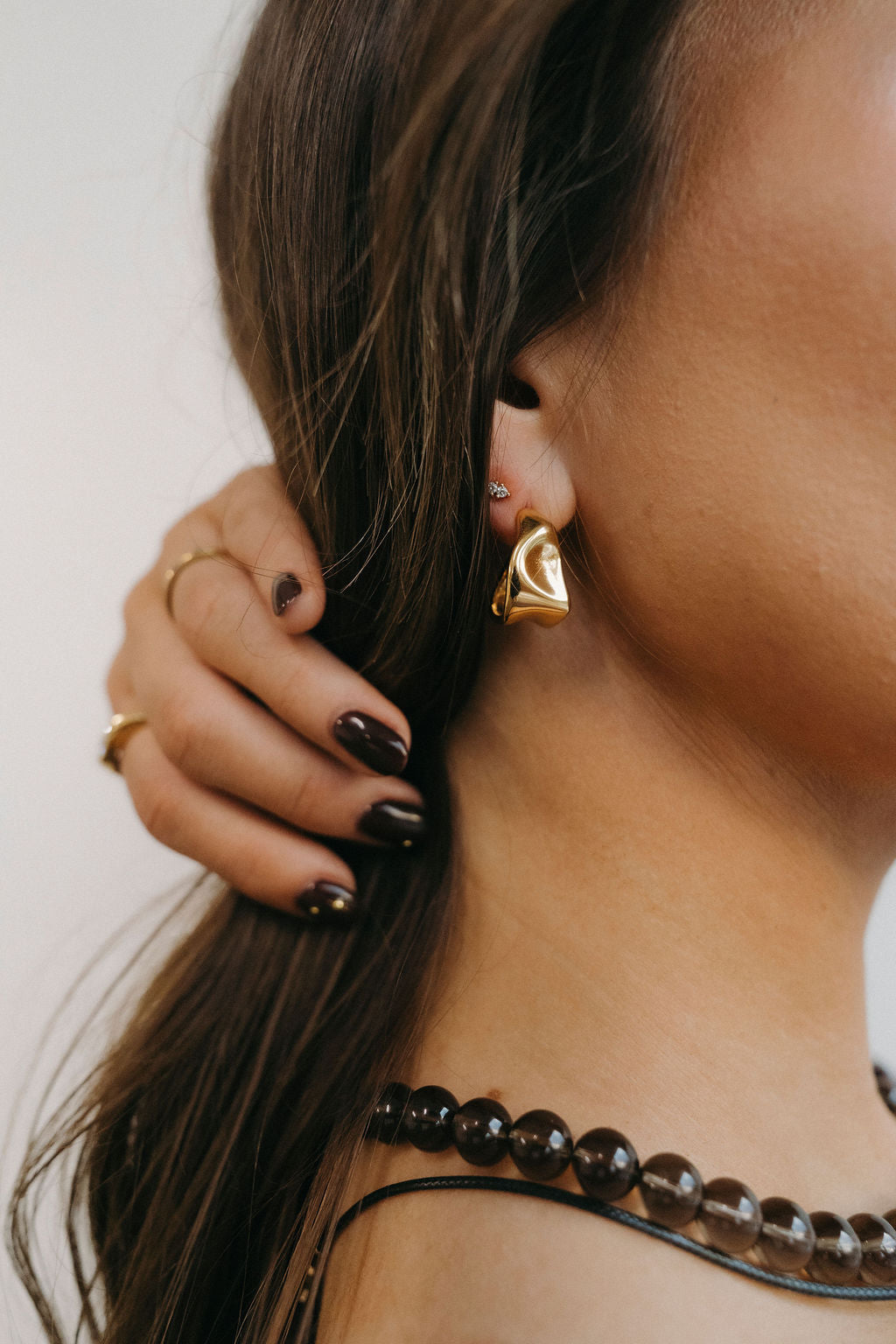 Close-up of a person wearing gold hoop earrings and a black beaded necklace.