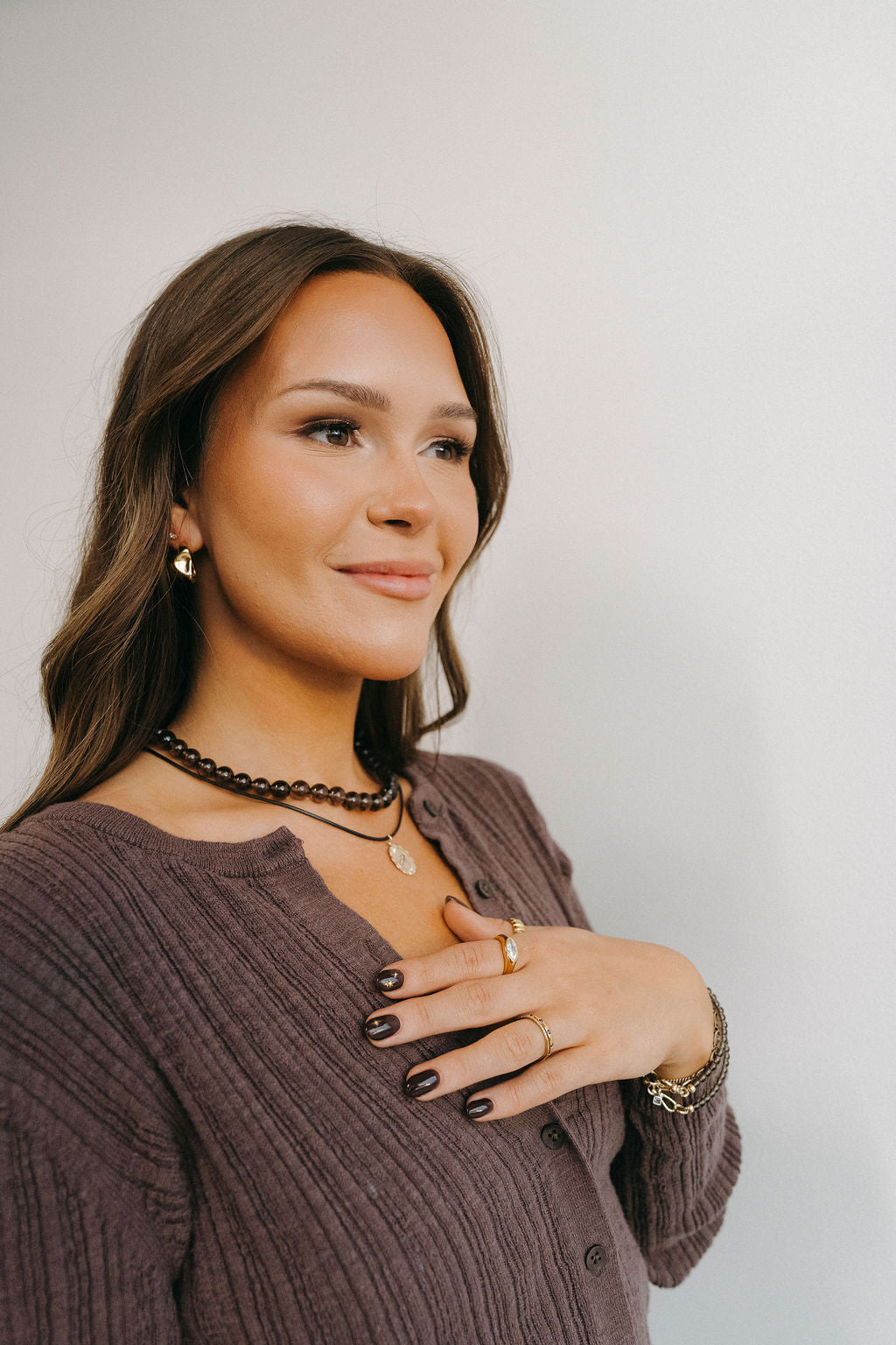 Woman wearing jewelry including a necklace, earrings, and rings against a plain background