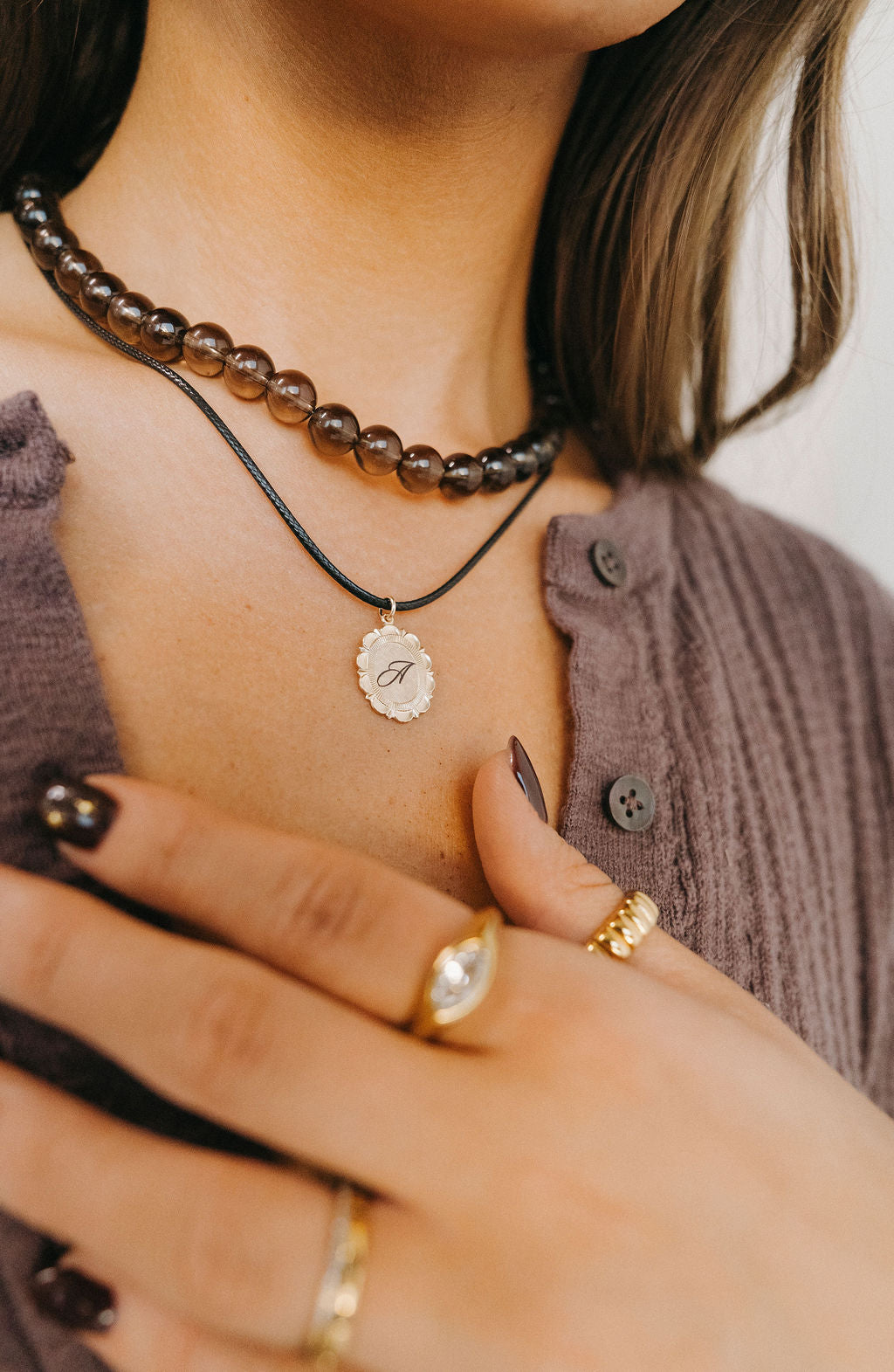 Close-up of a person wearing a necklace with a pendant, two rings on fingers, and a textured brown cardigan.