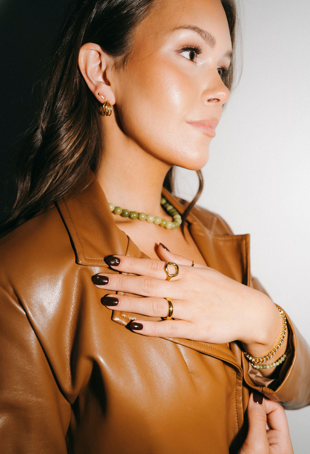 Woman wearing a brown leather jacket with jewelry, including rings and a necklace.