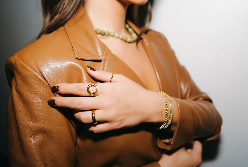 Person wearing a brown leather jacket with jewelry on a neutral background