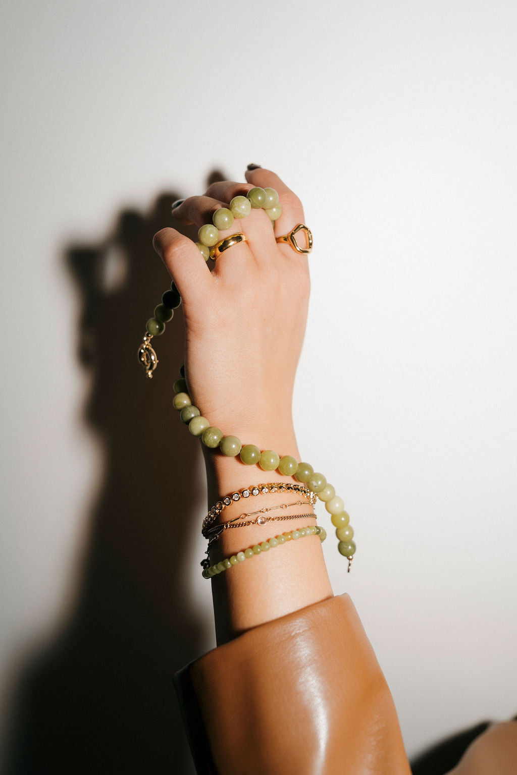 Hand wearing multiple green beaded bracelets on a neutral background