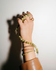 Hand wearing multiple green beaded bracelets on a neutral background