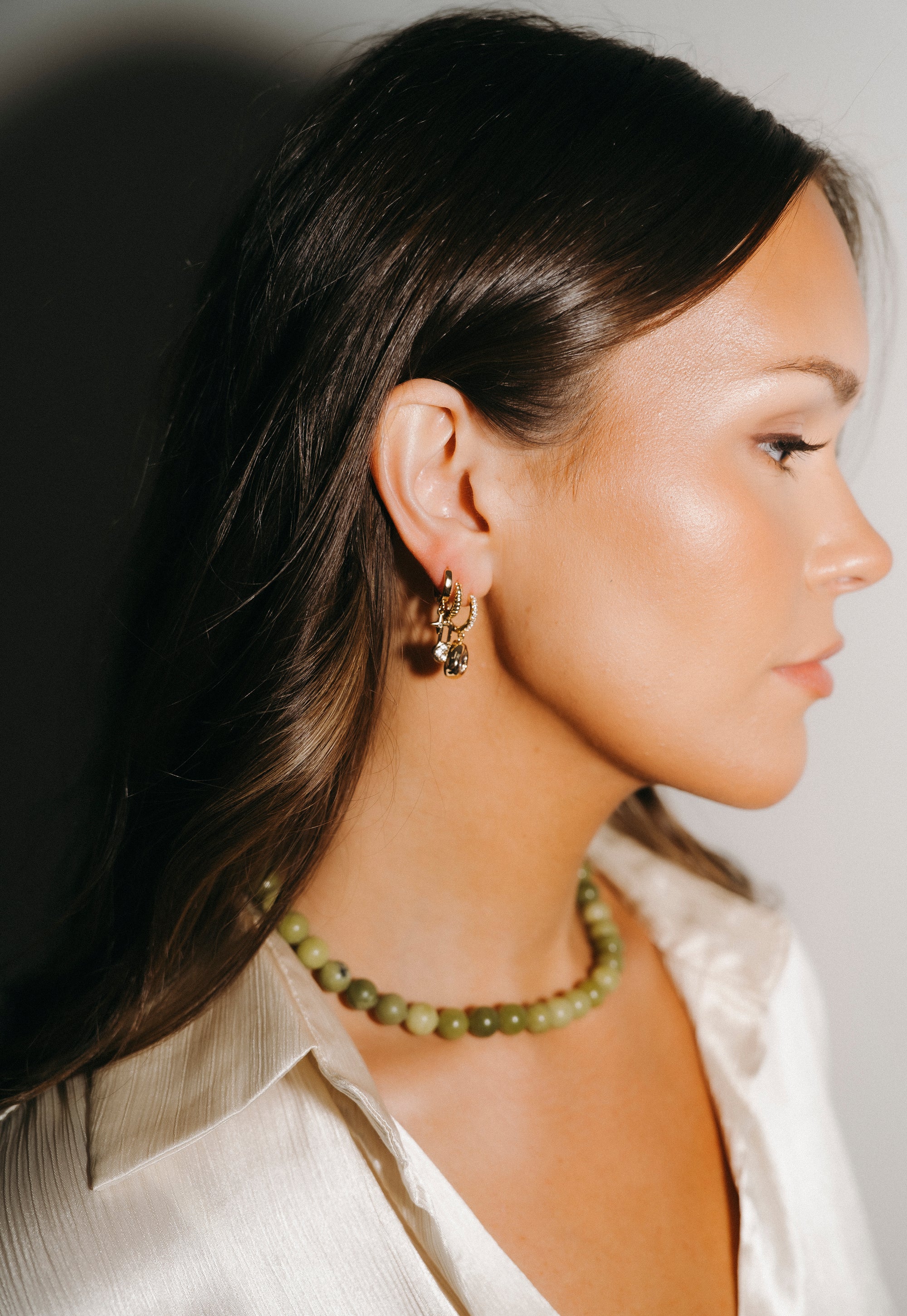 Woman wearing a green beaded necklace and gold earrings against a neutral background