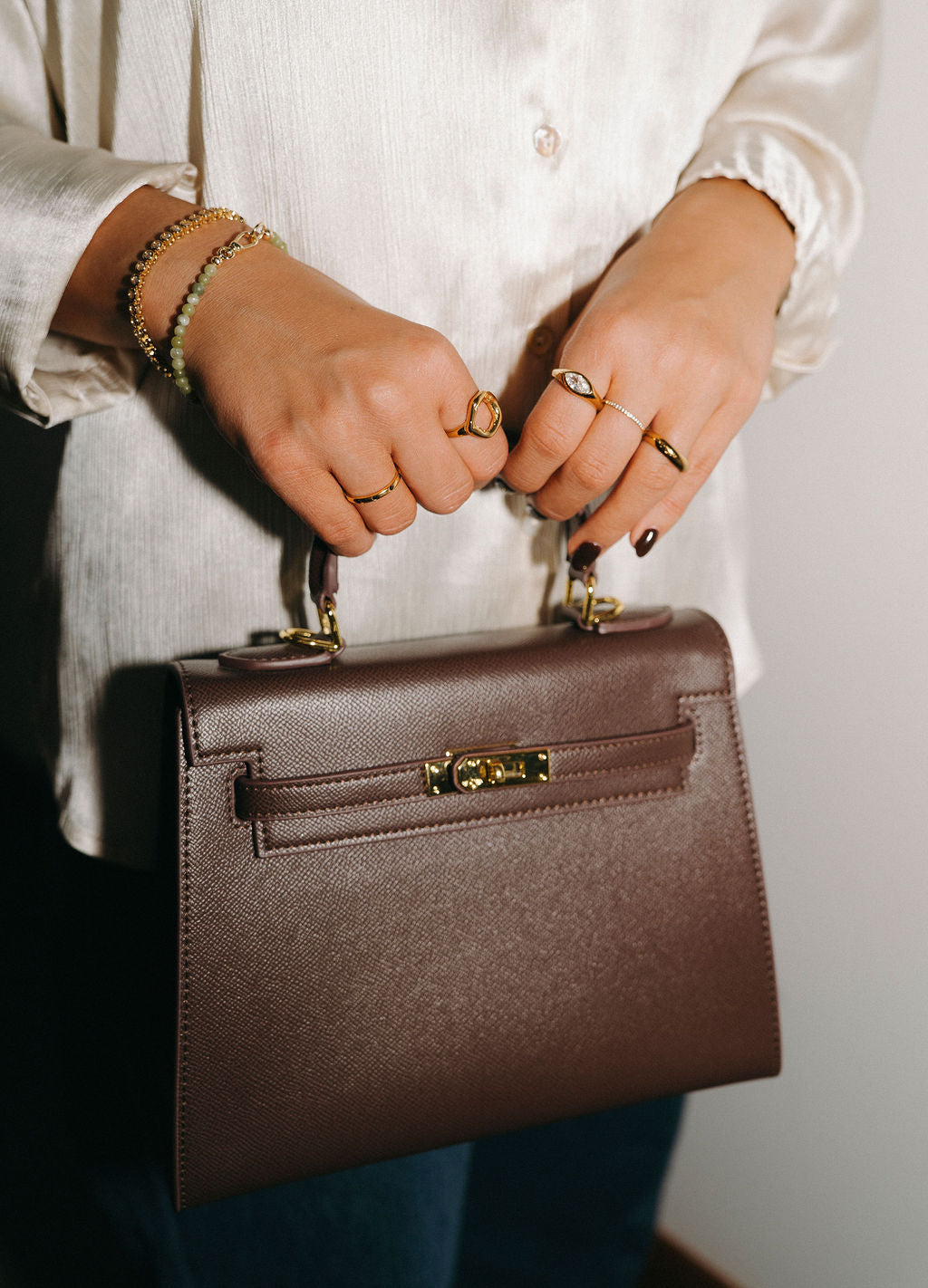 Person holding a brown handbag with gold accents against a neutral background