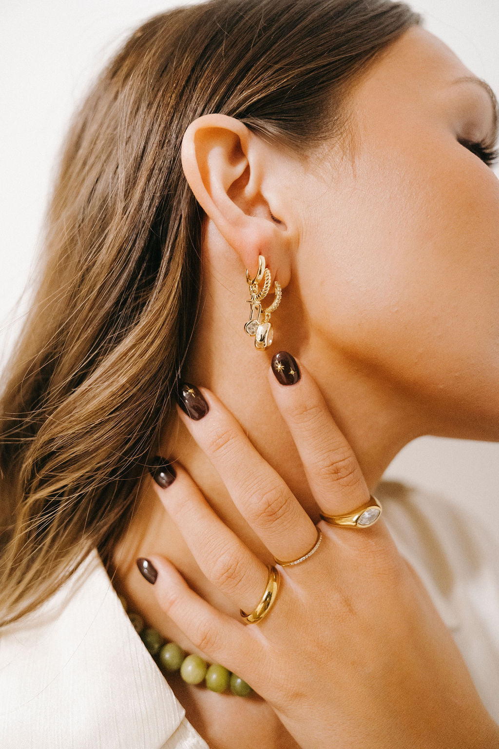 Close-up of a woman wearing gold hoop earrings and rings with a neutral background