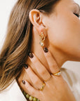 Close-up of a woman wearing gold hoop earrings and rings with a neutral background