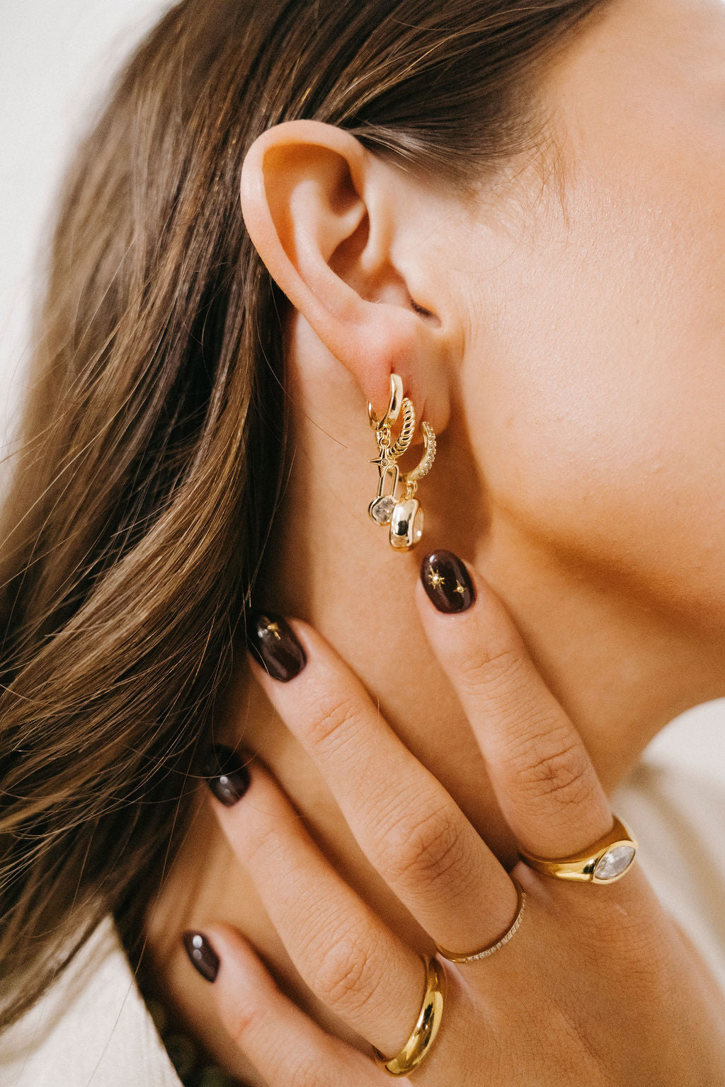 Close-up of a person wearing gold earrings and rings with a neutral background