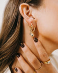 Close-up of a person wearing gold earrings and rings with a neutral background