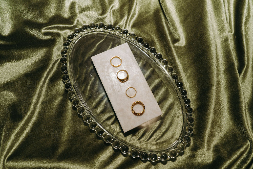 Set of gold rings on a white card inside an oval glass dish on a green velvet background