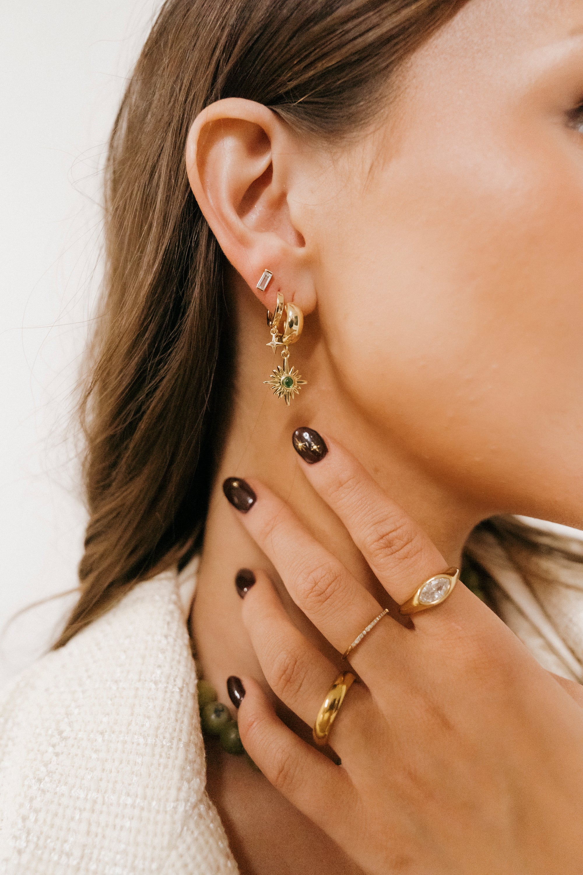 Close-up of a person wearing gold earrings and rings with a neutral background