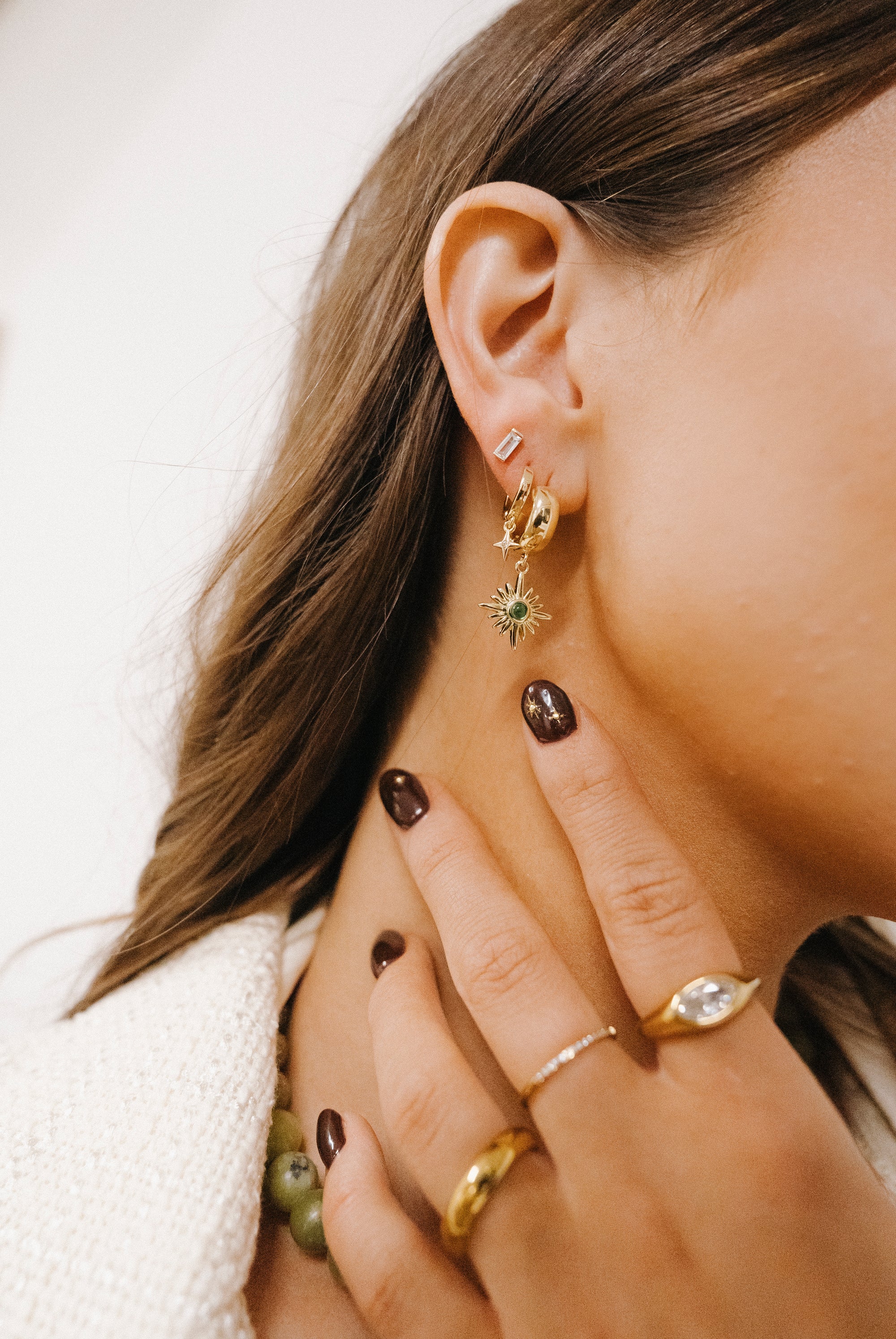 Close-up of a person wearing gold earrings and rings with a neutral background