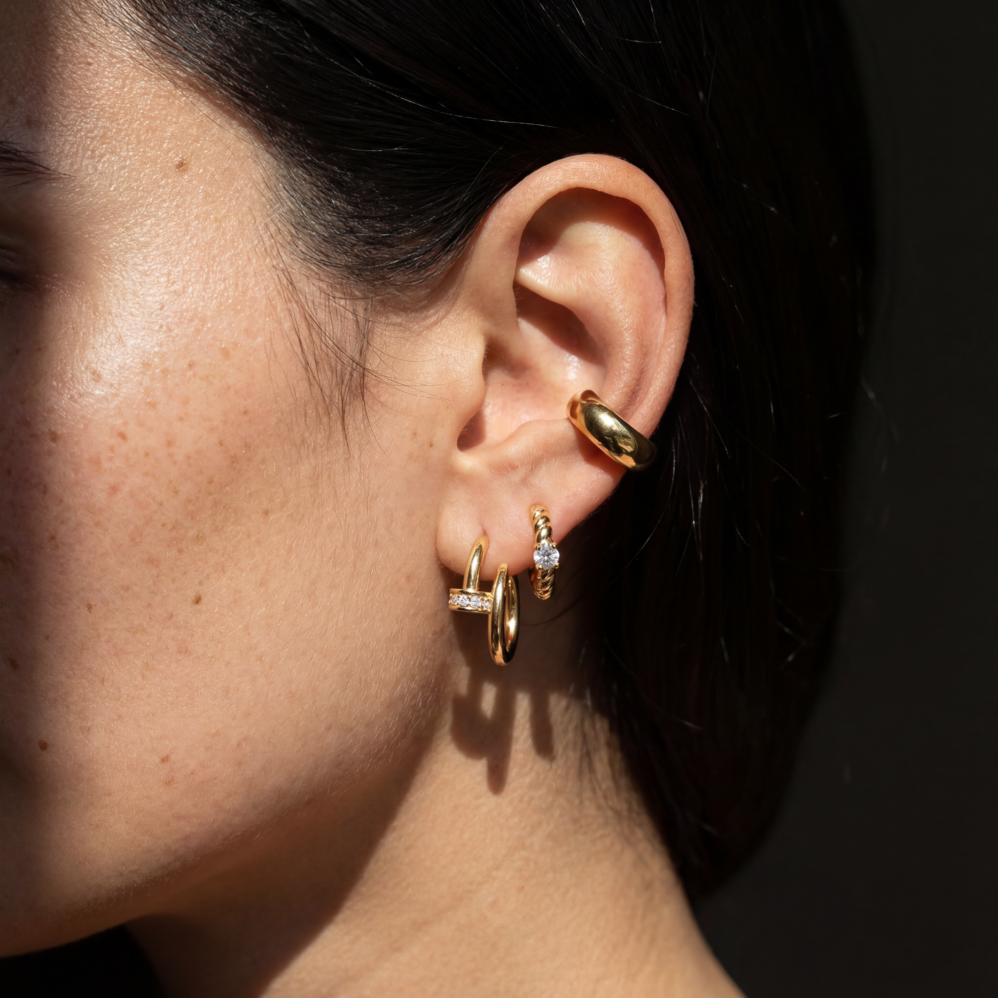 Close-up of an ear wearing gold hoop earrings with a dark background