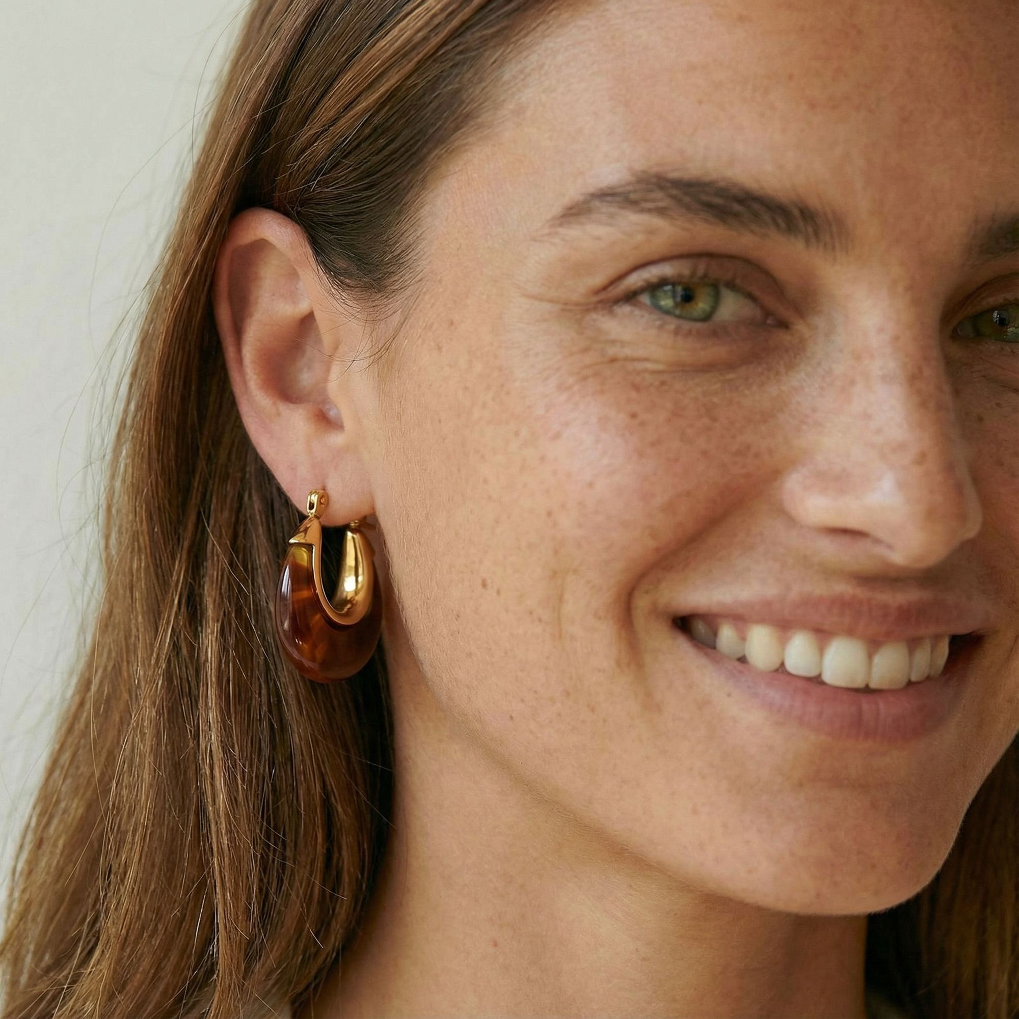 Close-up of a woman wearing gold hoop earrings with a neutral background
