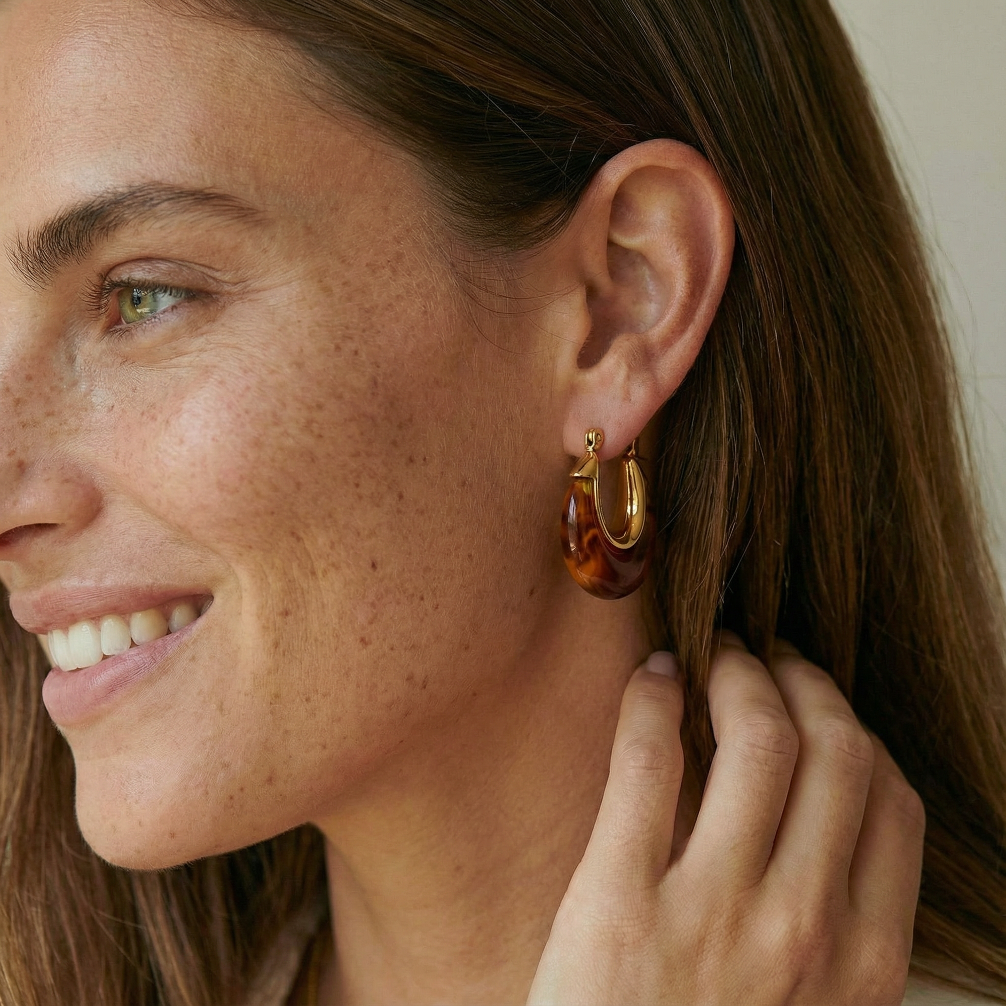 Woman wearing a tortoiseshell hoop earring with a neutral background