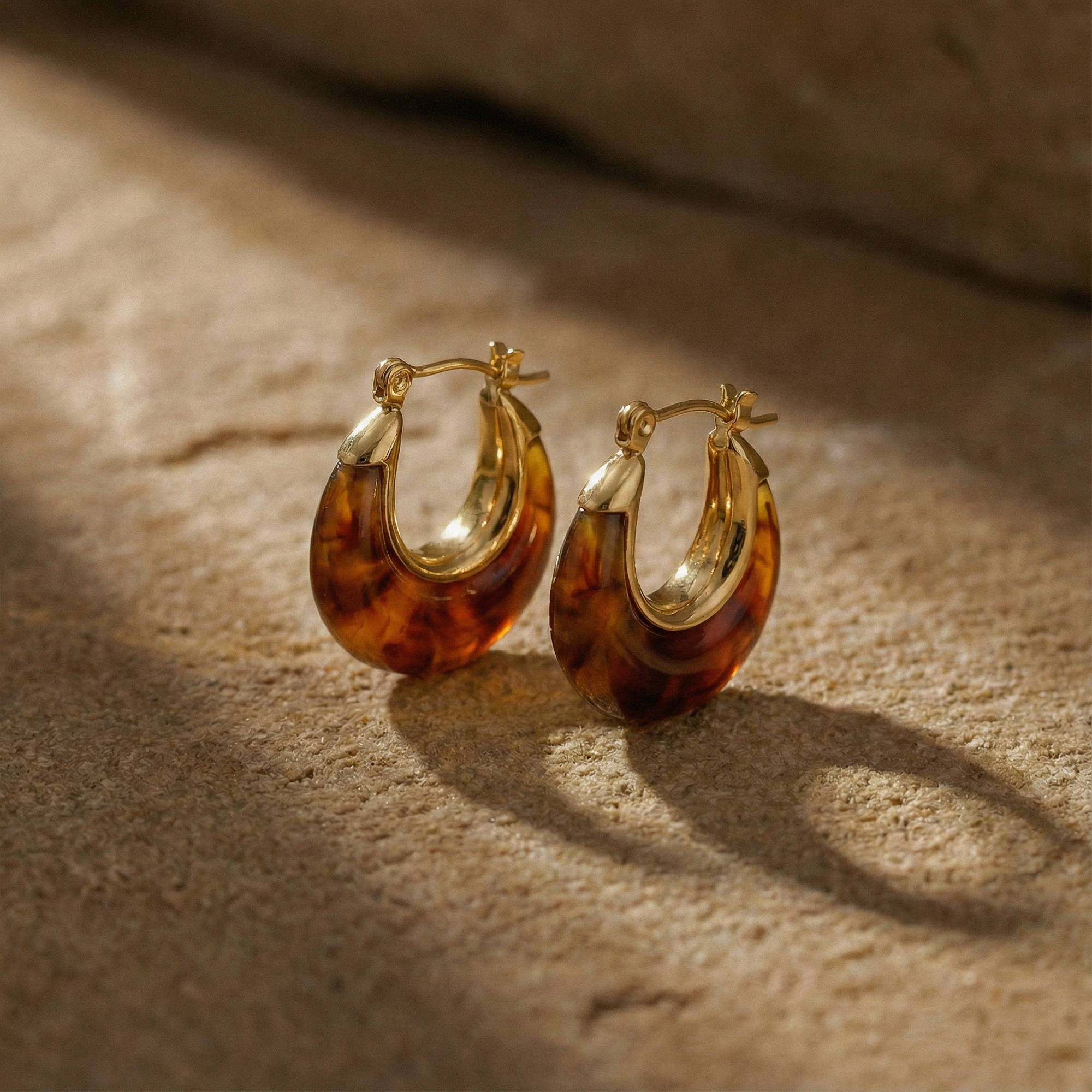 Tortoiseshell hoop earrings with gold accents on a textured beige surface