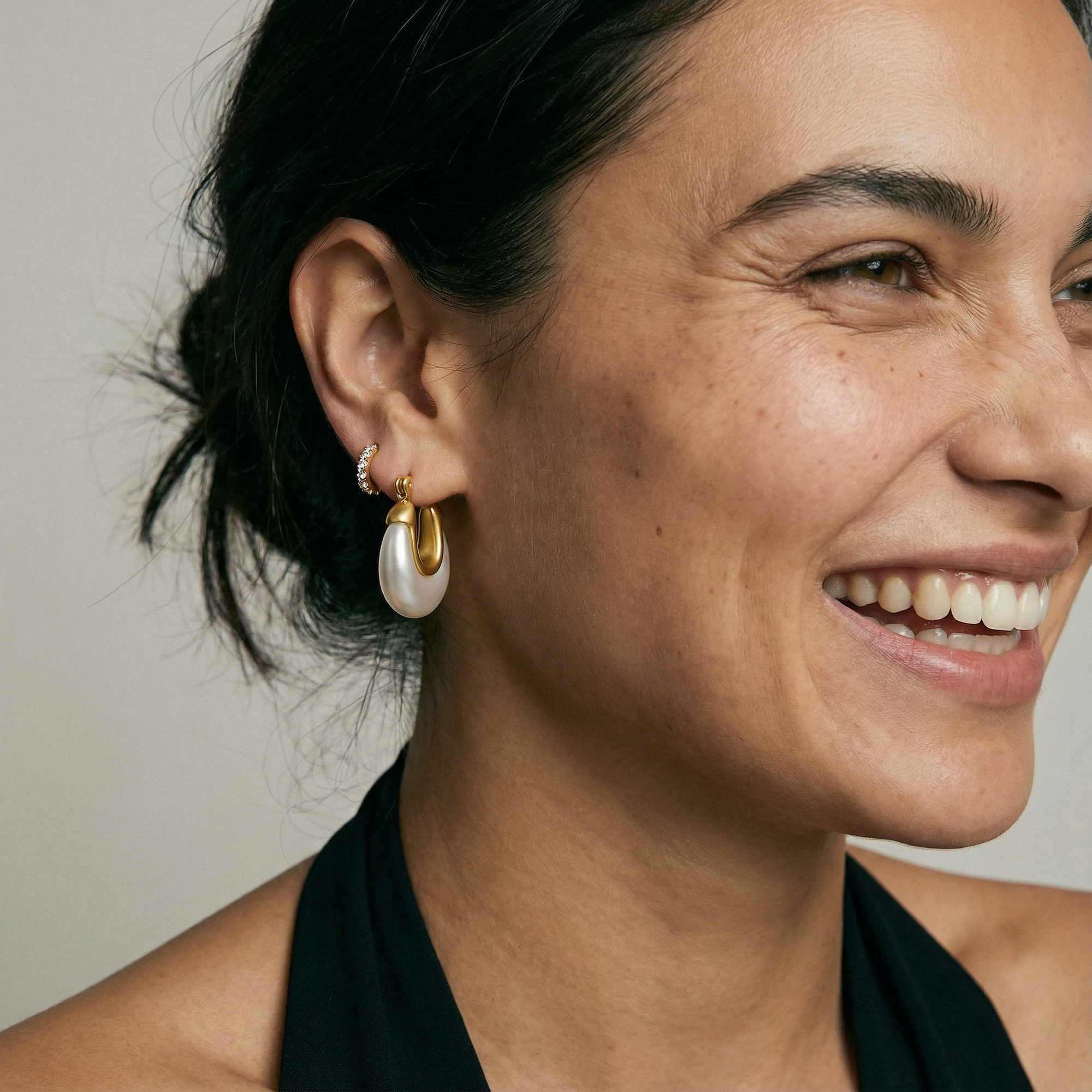Close-up of a woman wearing gold hoop earrings with a neutral background