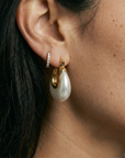 Close-up of an ear wearing a gold hoop earring with a pearl-like charm.