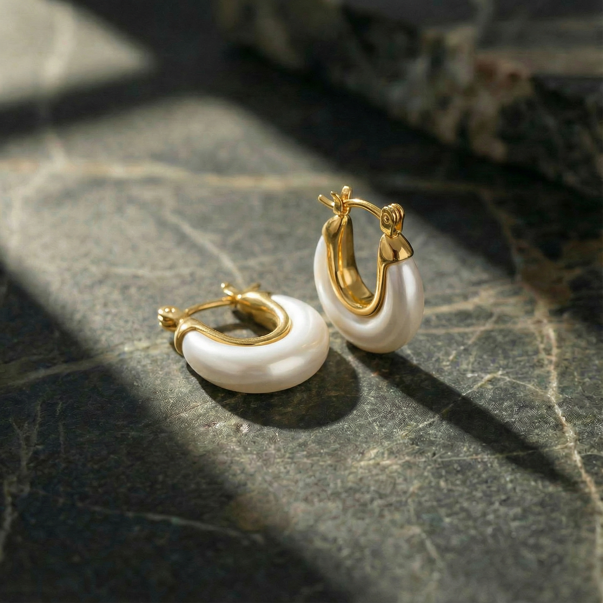Gold hoop earrings with white pearls on a dark stone surface