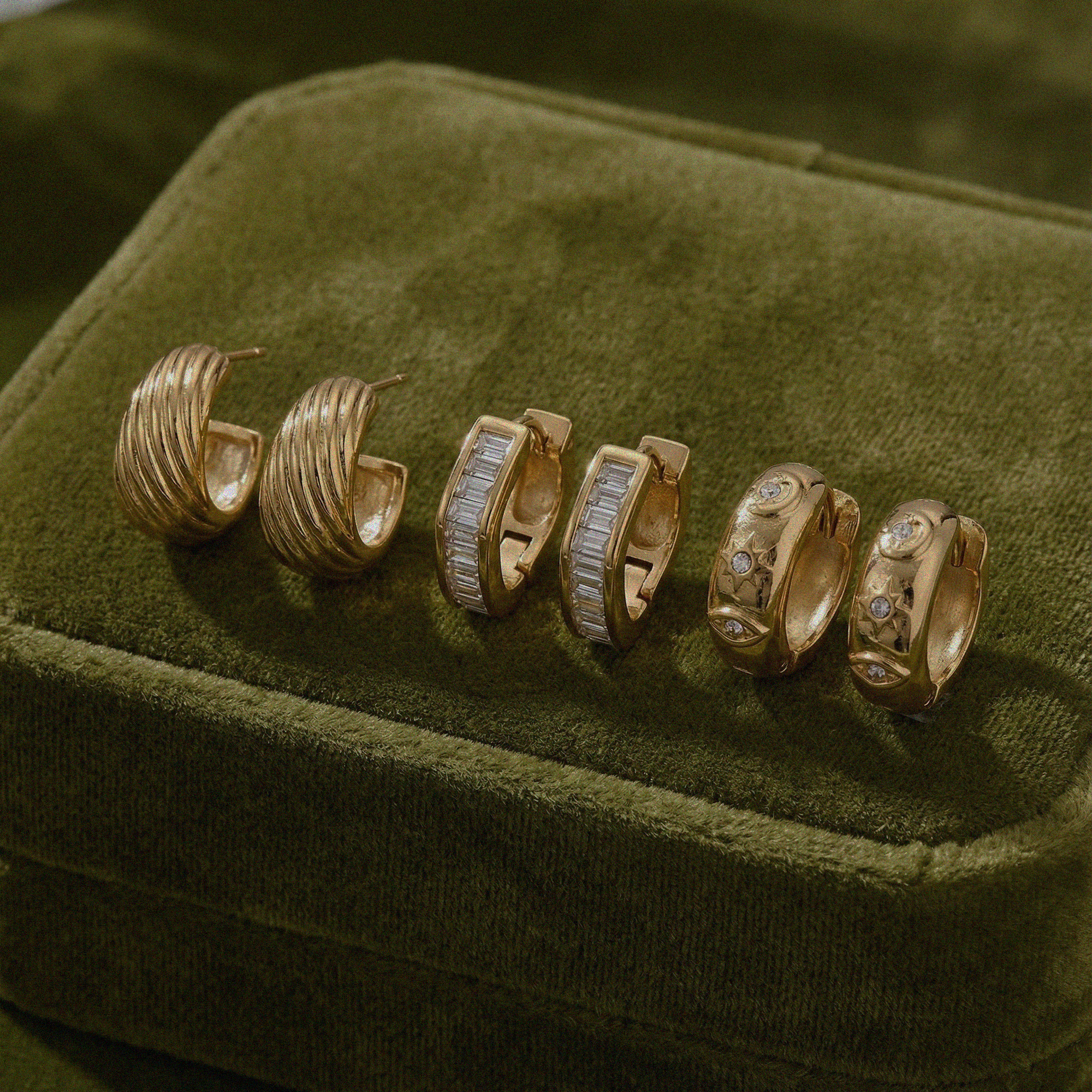 Set of gold hoop earrings with embedded stones on a green velvet surface