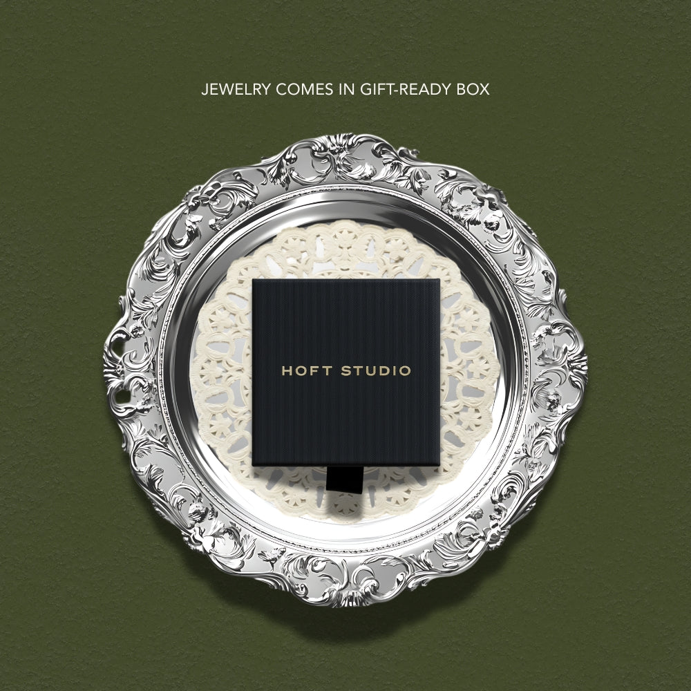 Decorative silver frame with a black square jewelry box displaying &#39;HOFT STUDIO&#39; on a green background. Each piece of jewelry comes packaged in a gift box.