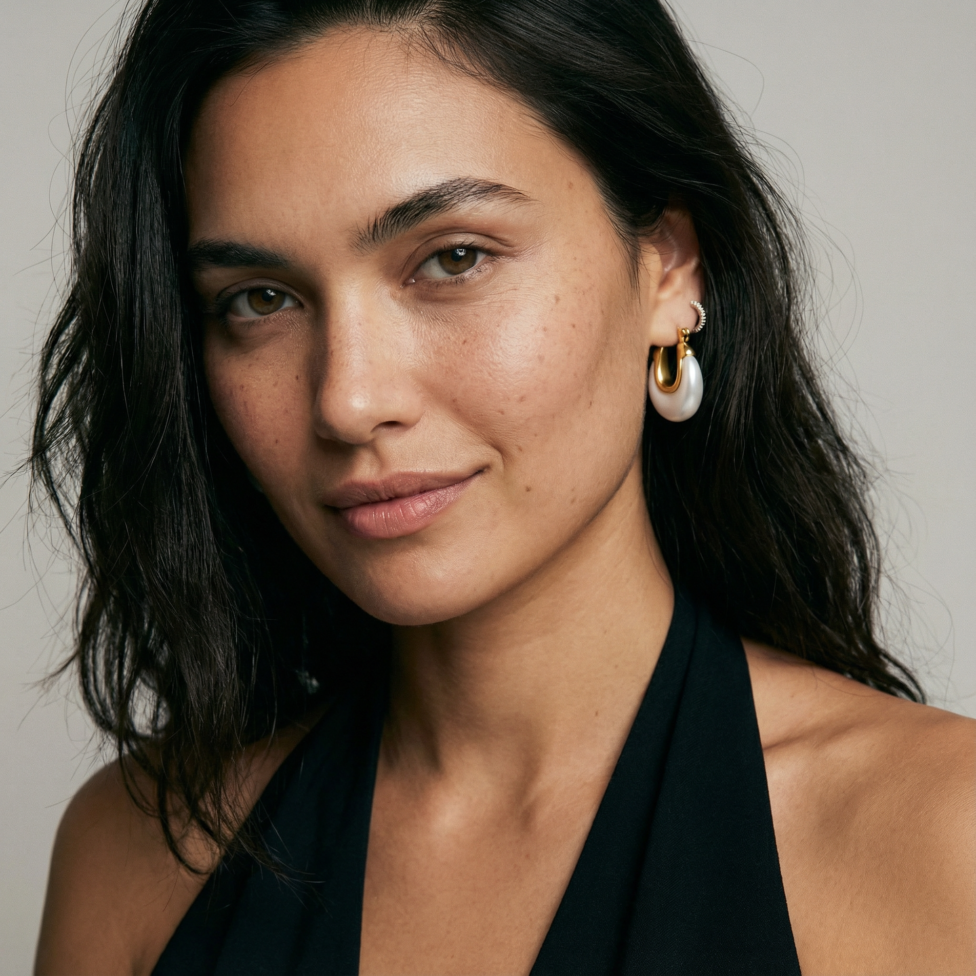 Woman wearing gold and pearl earrings against a neutral background